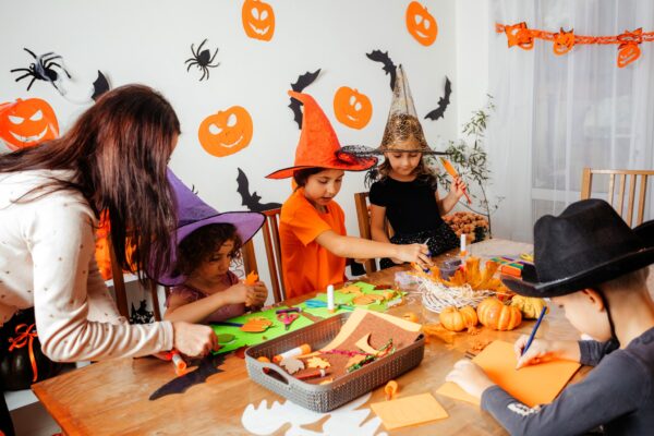 Halloween workshop for creative children. Teacher helps kids to make stylized paper bookmarks. Cheerful children spending time at Halloween party creating handmade products.