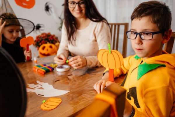 Portrait of cute smiling boy holding handmade paper pumpkin. Schoolboy demonstrates what he created during halloween workshop. Creative kids concept.