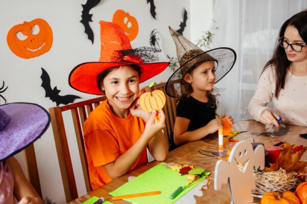 Cheerful and engaged schoolkids creating handmade bookmarks in halloween style during workshop. Teacher with children at wooden table making halloween decorations for school party.